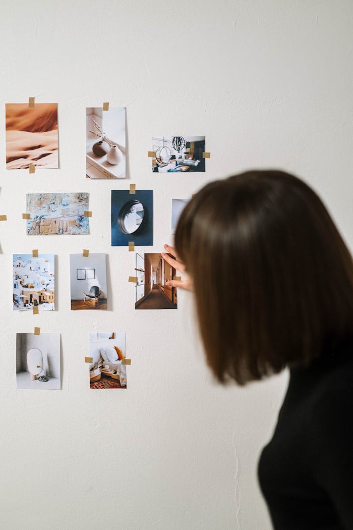 journey A woman arranges various art photographs on a light wall, creating a minimalistic display.